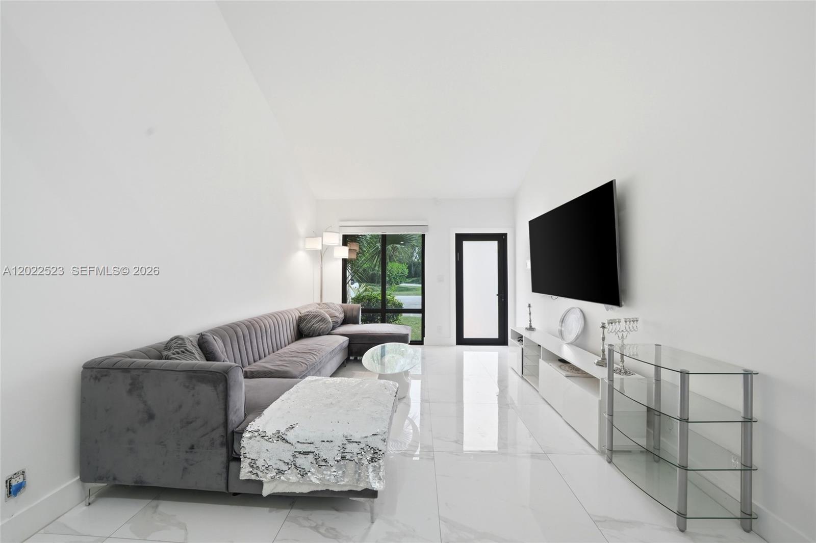 A modern living room features a grey sectional sofa, white tile floors, and a wall-mounted television — 455 NE 210th Ter, Miami FL 33179, MIAMI, FL