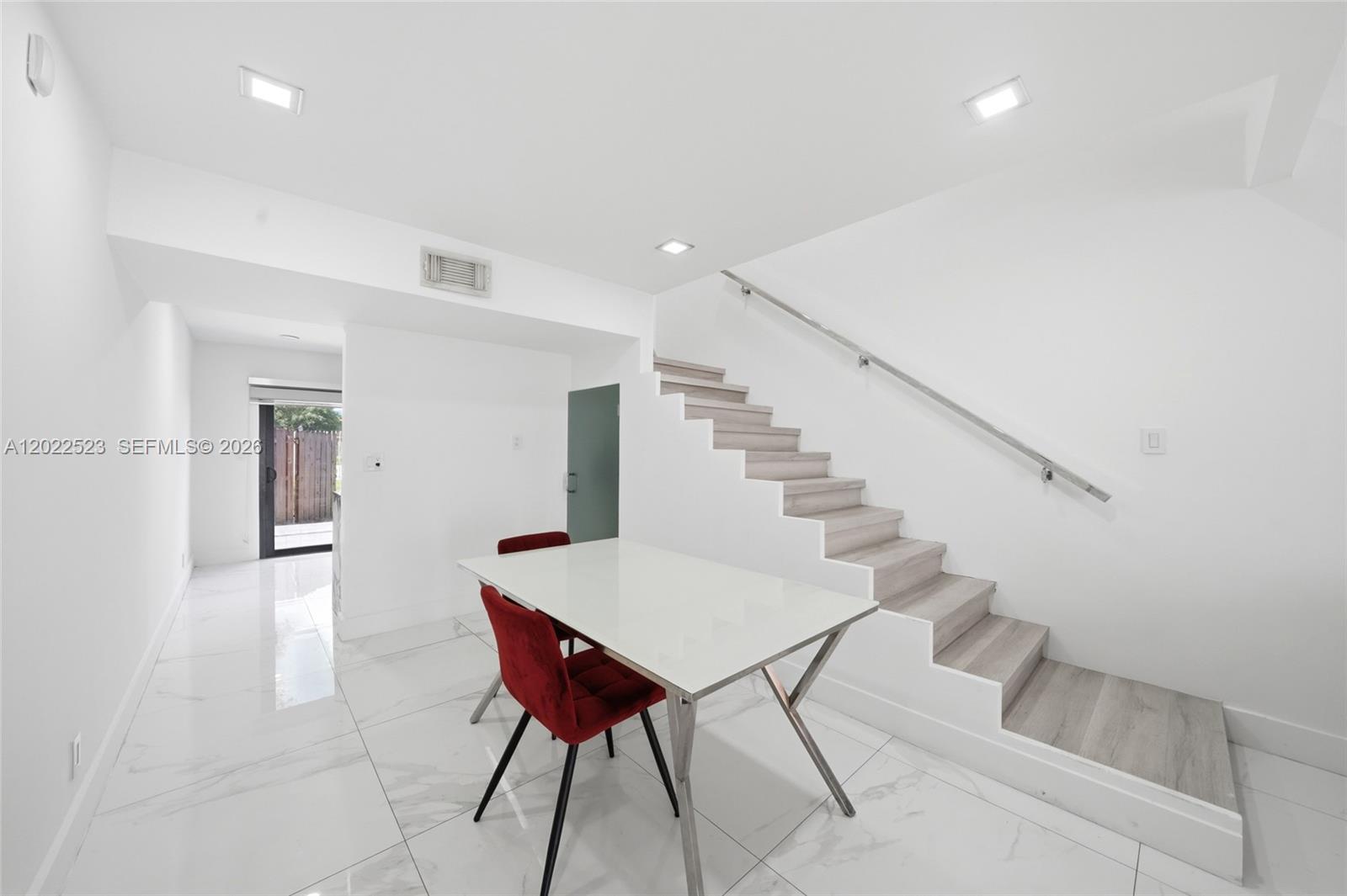A dining area features white tile floors, a modern table, and stairs with wood treads — 455 NE 210th Ter, Miami FL 33179, MIAMI, FL