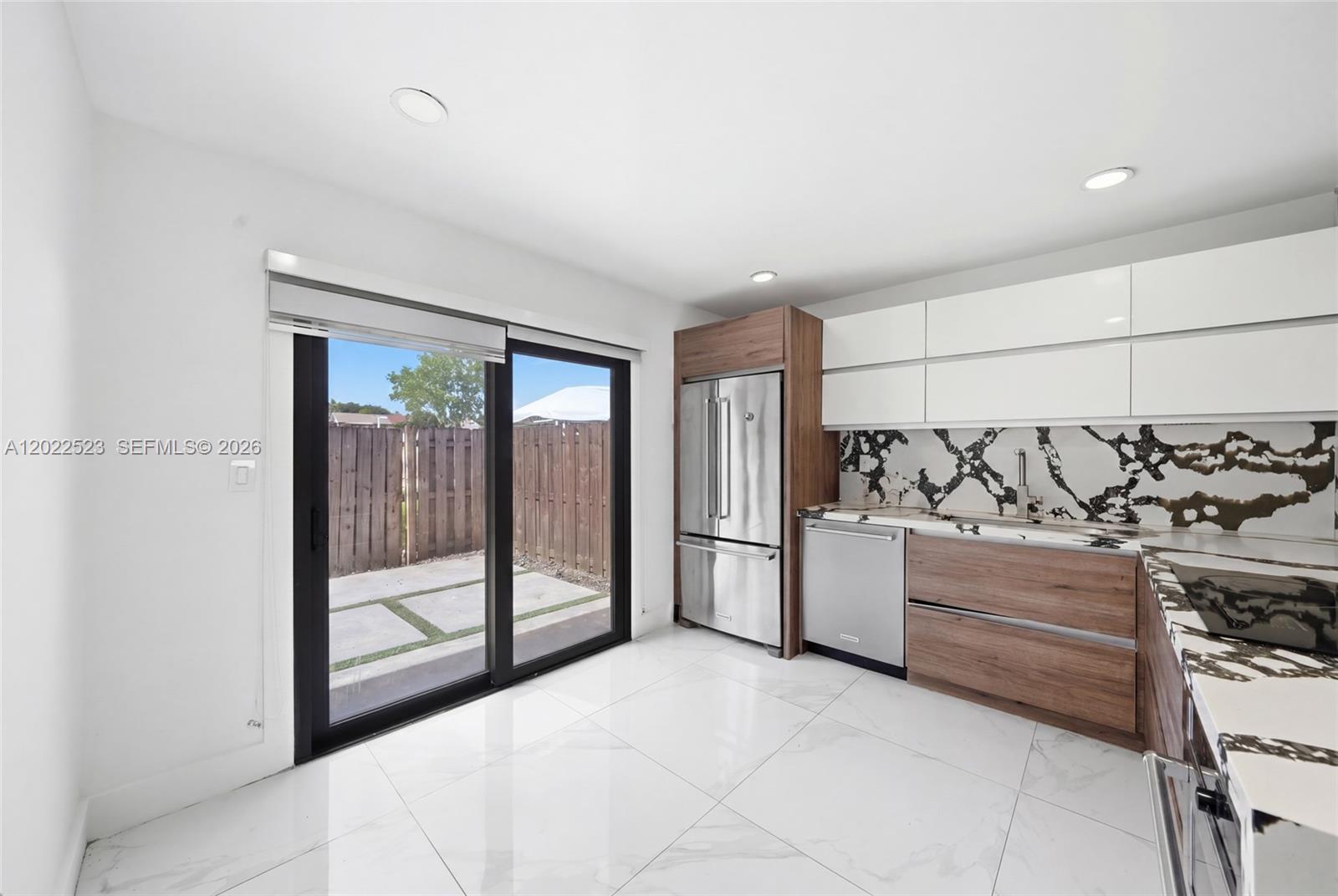 A modern kitchen features white cabinets, wood-toned lower drawers, marble-patterned countertops, and a sliding glass door — 455 NE 210th Ter, Miami FL 33179, MIAMI, FL