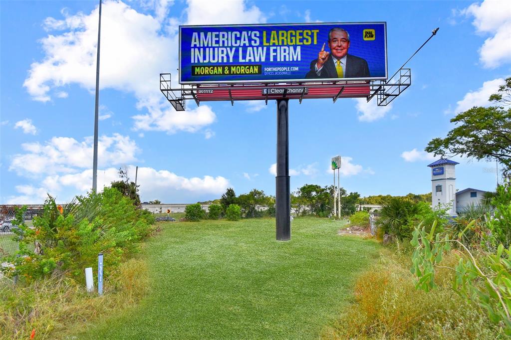 A large billboard for a law firm stands in a grassy field under a blue sky — 7268 MORSE AVENUE, JACKSONVILLE, FL