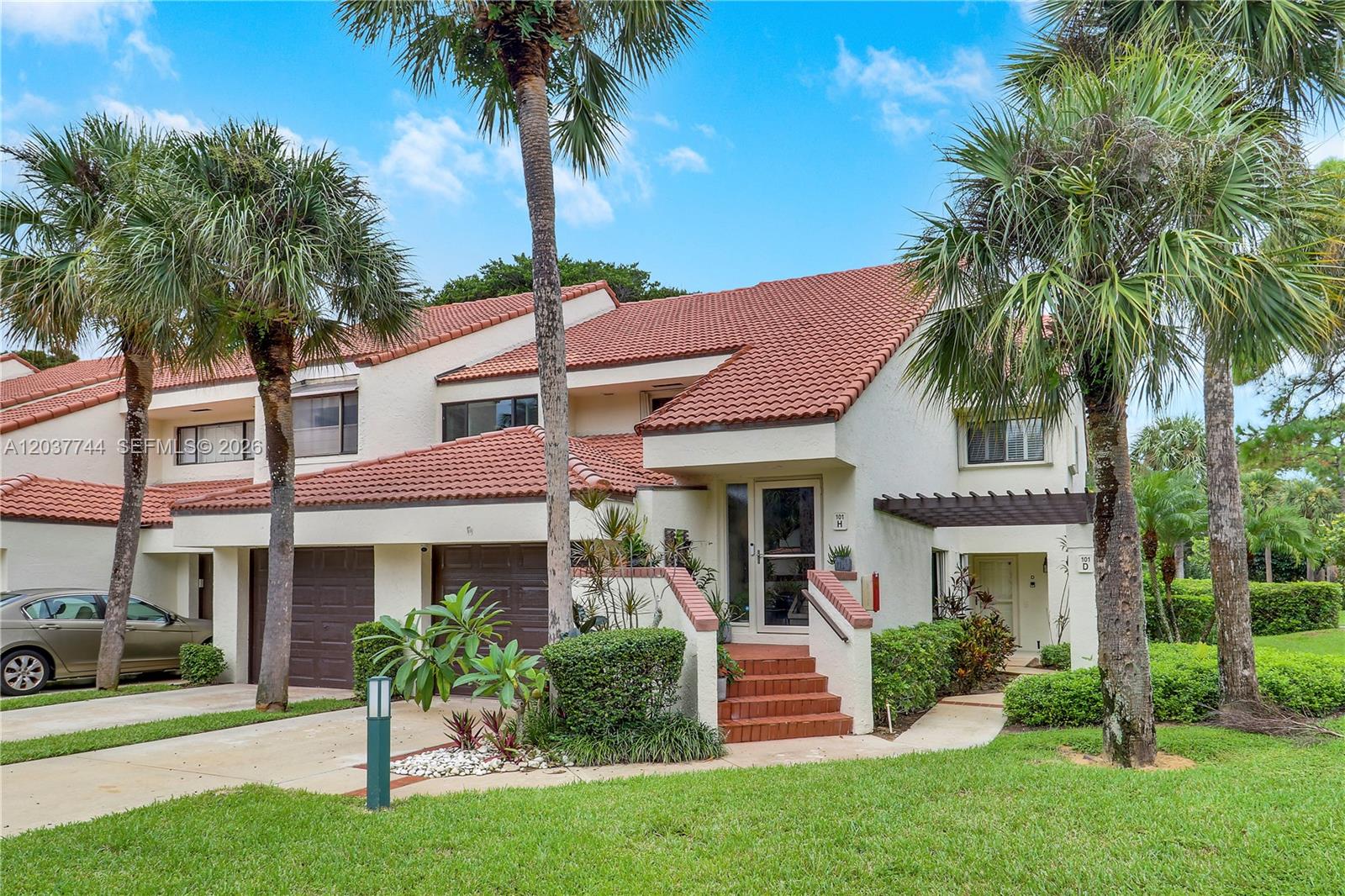 A two-story townhouse with a red tile roof, brown garage doors, and palm trees — 101 Sea Oats Dr # H, Juno Beach FL 33408, JUNO BEACH, FL