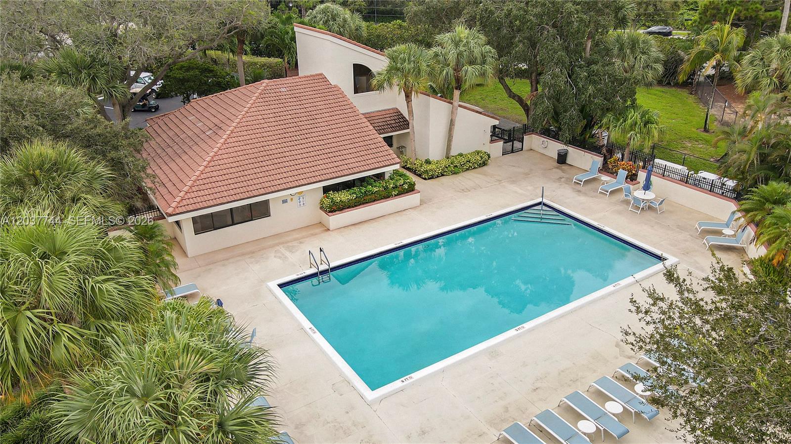 An aerial view shows a rectangular swimming pool next to a building with a tiled roof — 101 Sea Oats Dr # H, Juno Beach FL 33408, JUNO BEACH, FL