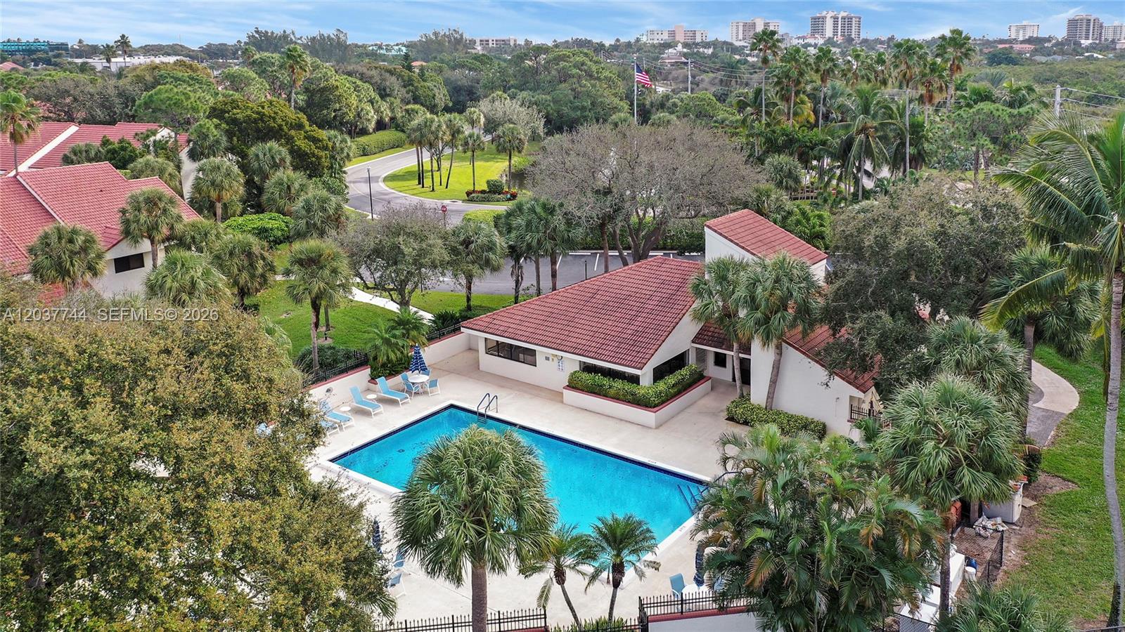 An aerial view shows a swimming pool and clubhouse surrounded by palm trees and landscaping — 101 Sea Oats Dr # H, Juno Beach FL 33408, JUNO BEACH, FL