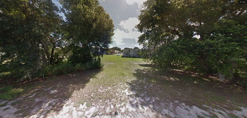 A grassy, vacant lot framed by large trees leads toward a distant building and street — 60 E STREET, LAKE WALES, FL