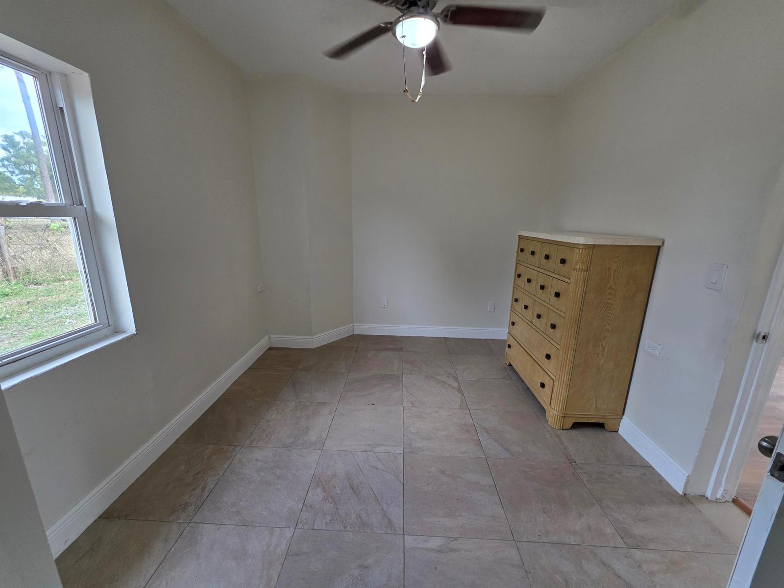 A room with light-colored walls, tile flooring, a ceiling fan, and a wooden dresser — 15427 San Diego Drive, FL 33470, FL