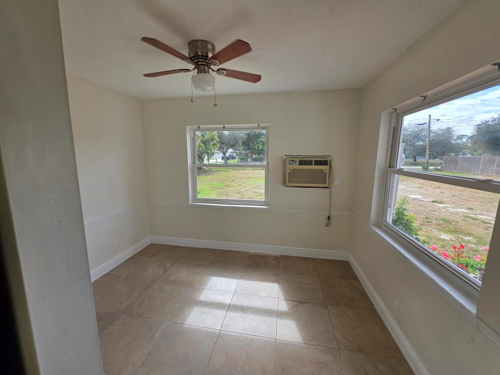 An empty room features tile flooring, a ceiling fan, two windows, and a wall-mounted air conditioner — 15427 San Diego Drive, FL 33470, FL