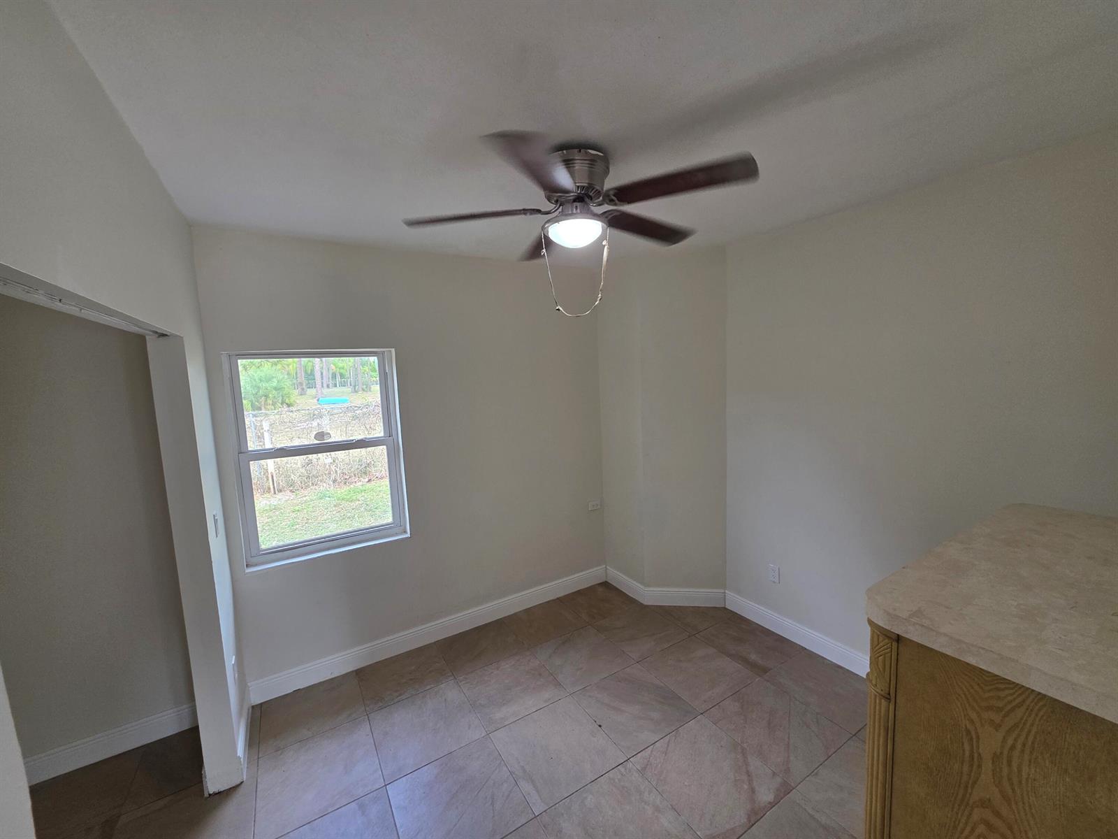 A small room with beige tile flooring, a ceiling fan, and a single window — 15427 San Diego Drive, FL 33470, FL