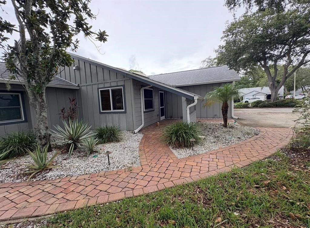 A gray house with vertical siding features a brick paver walkway leading to the entrance — 39650 US HIGHWAY 19 N UNIT 441, TARPON SPRINGS, FL