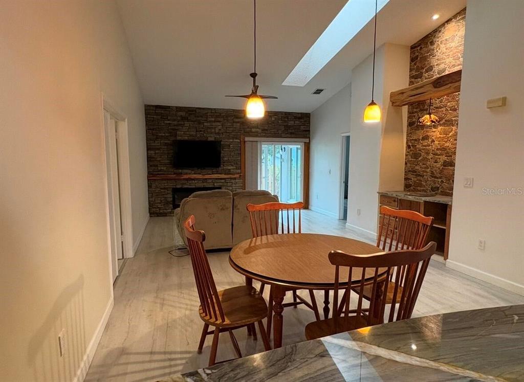 A dining area with a round wooden table sits before a living room with stone walls — 39650 US HIGHWAY 19 N UNIT 441, TARPON SPRINGS, FL