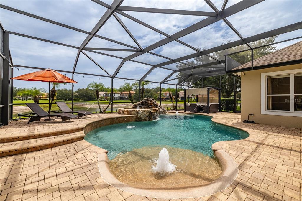 A screened-in patio features a swimming pool with a rock waterfall, fountain, and lounge chairs — 8016 CYPRESS CROSSING COURT, TAMPA, FL