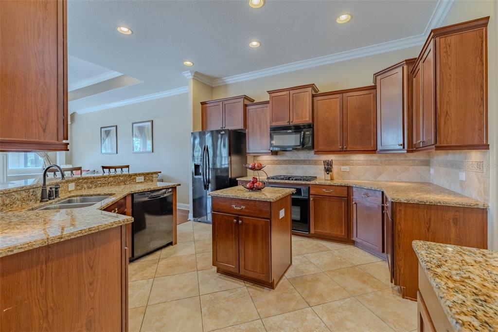 A kitchen features wood cabinets, granite countertops, a center island, and tile flooring — 8016 CYPRESS CROSSING COURT, TAMPA, FL