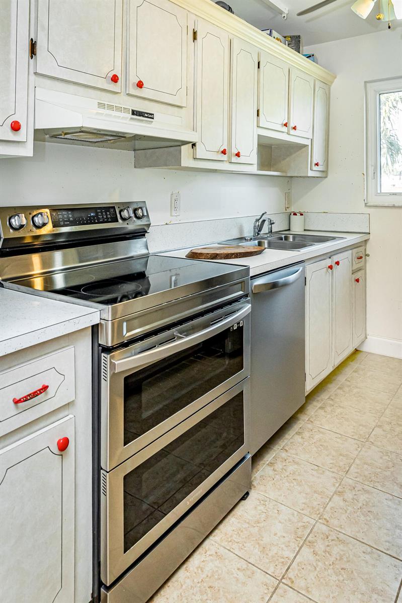 A kitchen features white cabinets with red knobs, stainless steel appliances, and light tile flooring — 310 Main Boulevard # C, Boynton Beach FL 33435, BOYNTON BEACH, FL