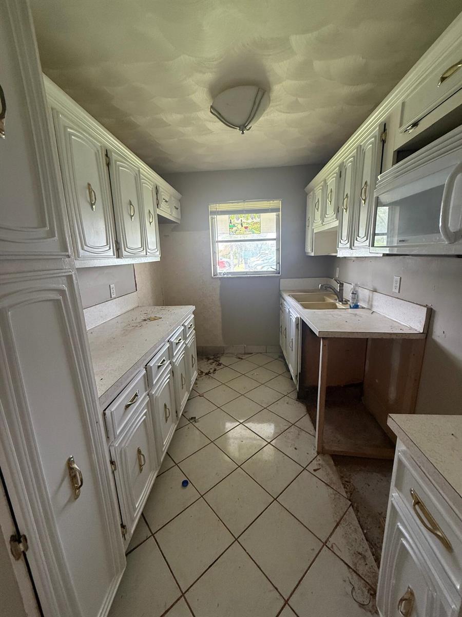 A galley-style kitchen features white cabinets, laminate countertops, tiled floors, and a single window — 1052 North Drive # B, Delray Beach FL 33445, DELRAY BEACH, FL