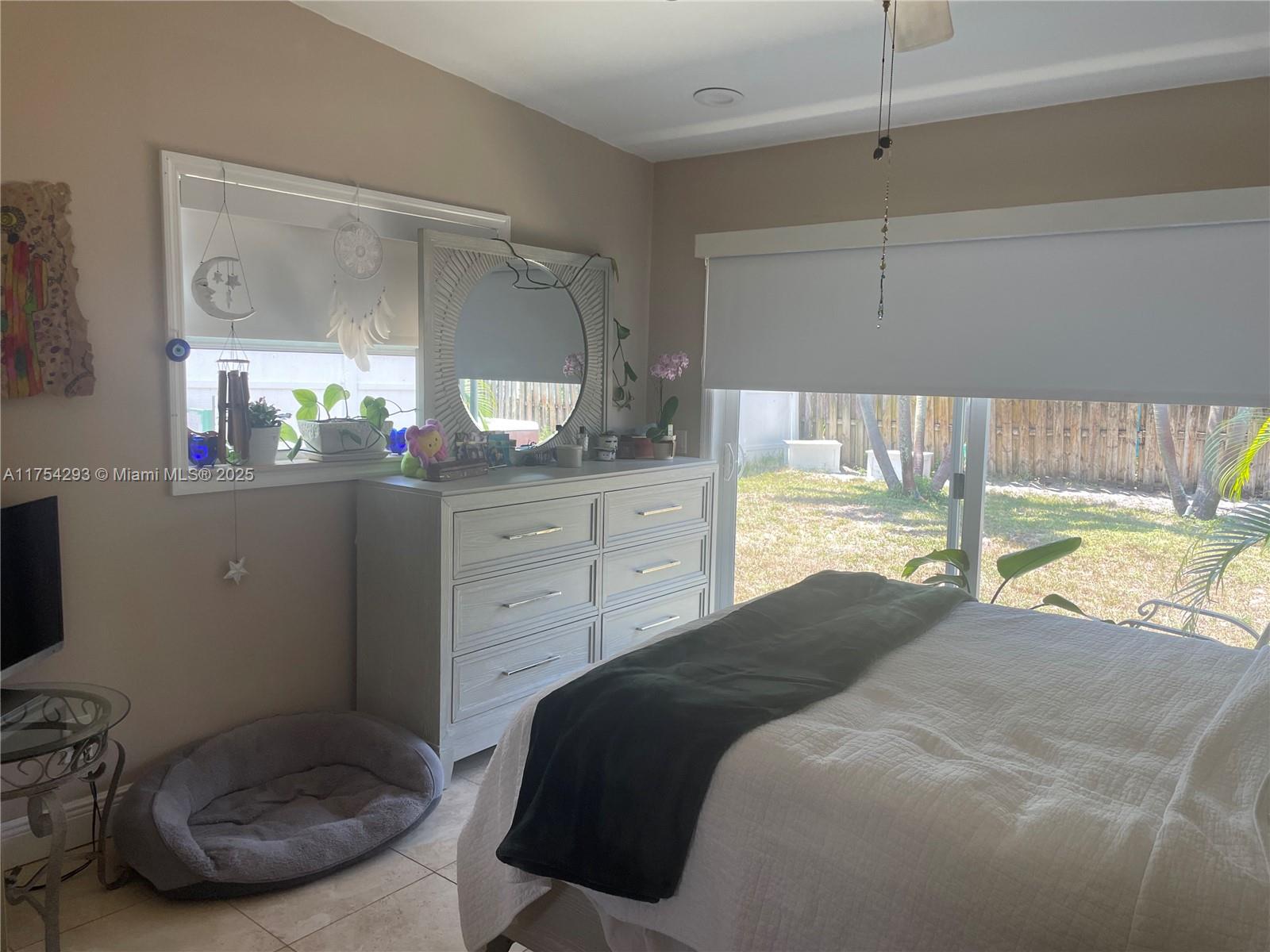 A bedroom features a light-colored dresser with a round mirror, a bed, and sliding doors — 18986 SE Mayo Dr, Jupiter FL 33469, JUPITER, FL
