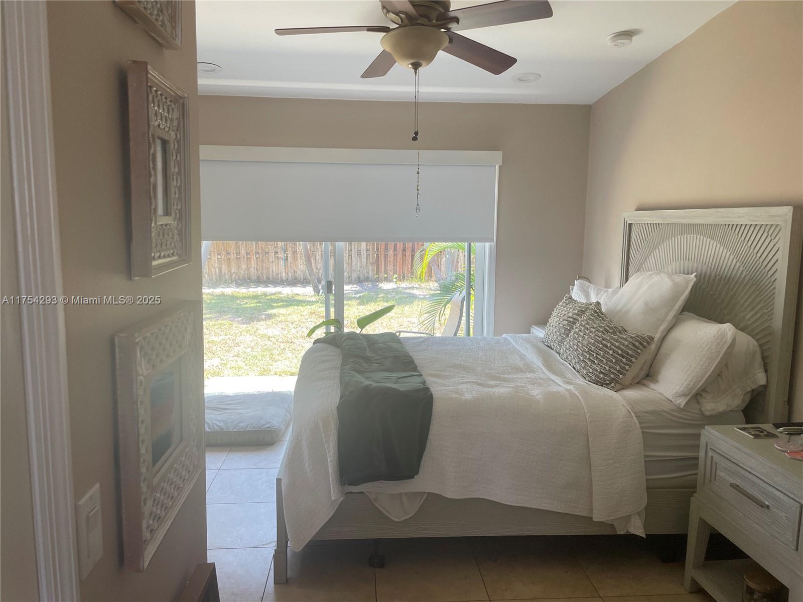 A bedroom features a bed with white bedding, a ceiling fan, and a sliding glass door — 18986 SE Mayo Dr, Jupiter FL 33469, JUPITER, FL