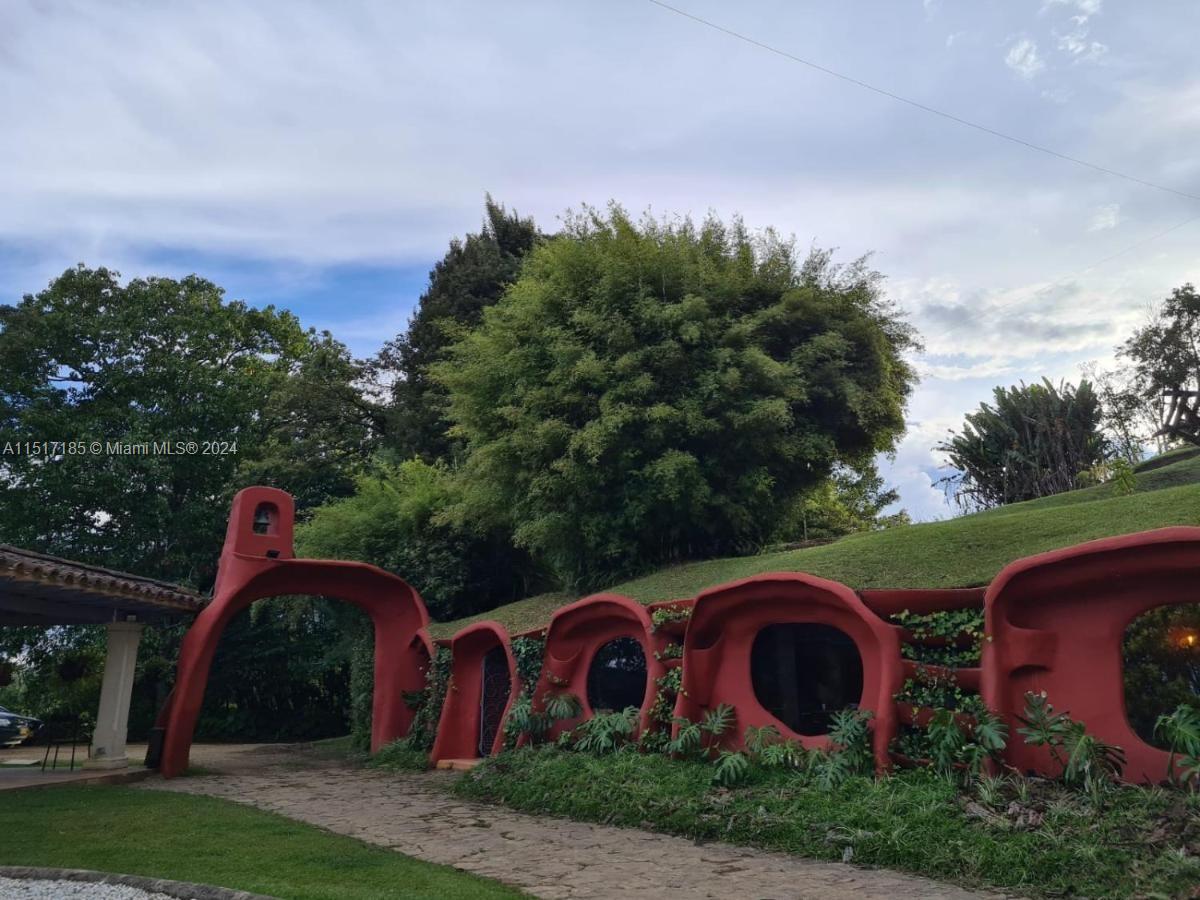 A unique, red-painted, earth-sheltered structure with arched openings sits along a stone path — 1 CIGARRALES DE SANTA TERESA, An, An