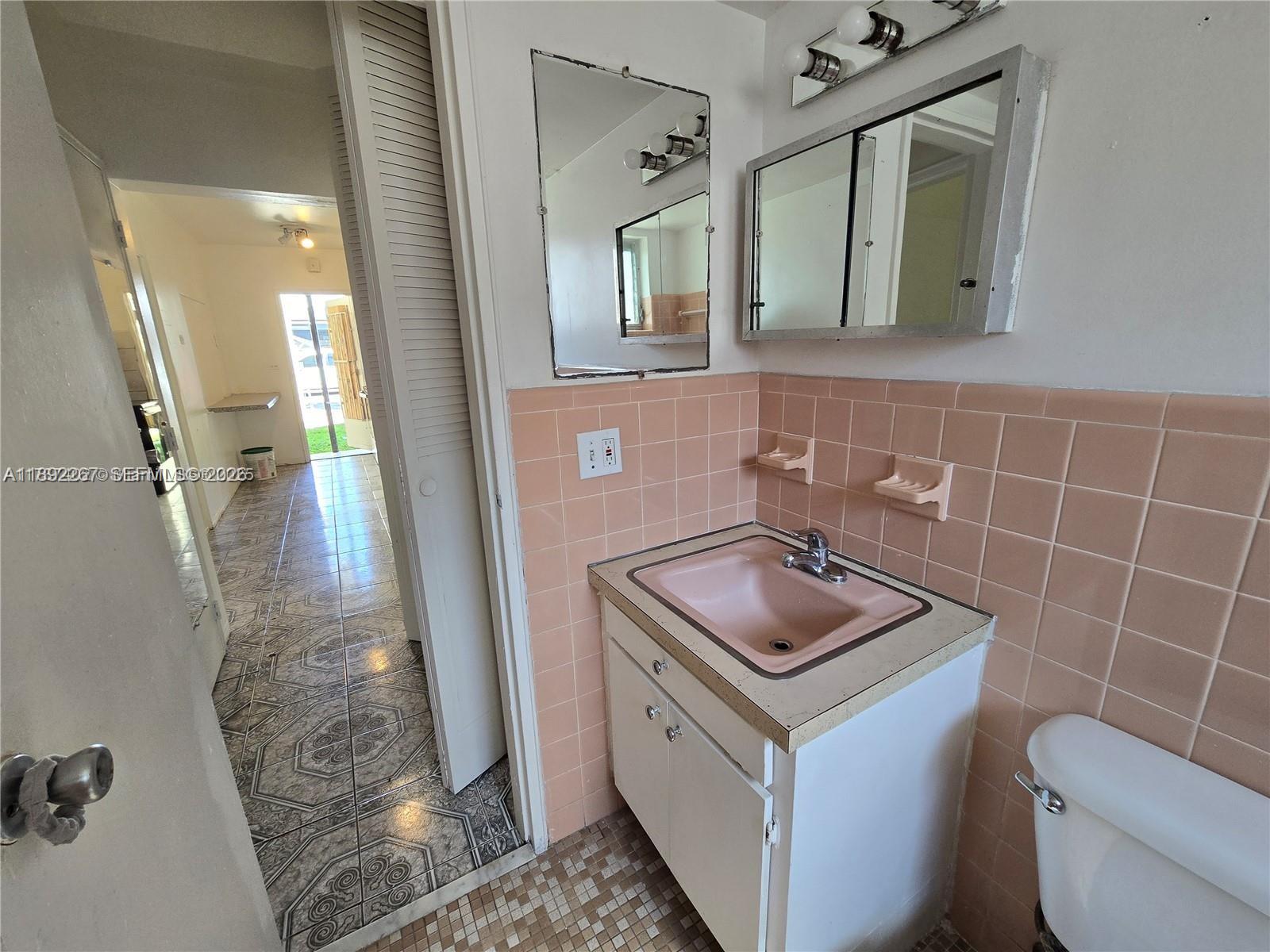 A bathroom features a pink sink, matching wall tiles, and a view into an adjacent room — 70 NW 77th St # 11, Miami FL 33150, MIAMI, FL