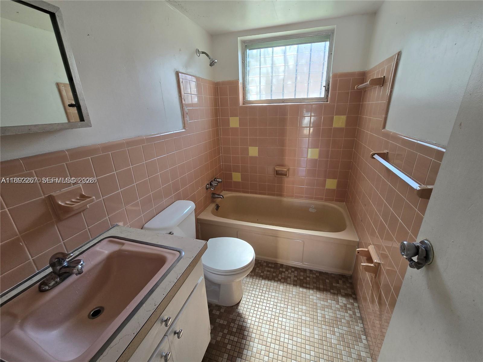 A bathroom features pink wall tiles, a matching pink sink, and a beige bathtub — 70 NW 77th St # 11, Miami FL 33150, MIAMI, FL