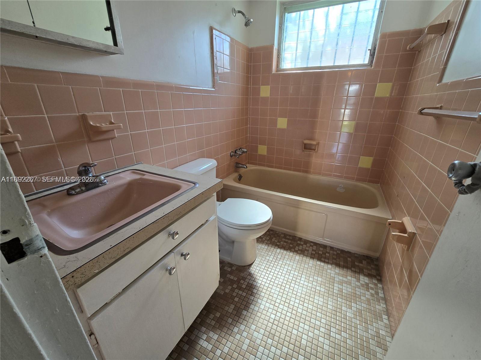 A bathroom features pink wall tiles, a pink sink, a beige bathtub, and mosaic floor tiles — 70 NW 77th St # 11, Miami FL 33150, MIAMI, FL