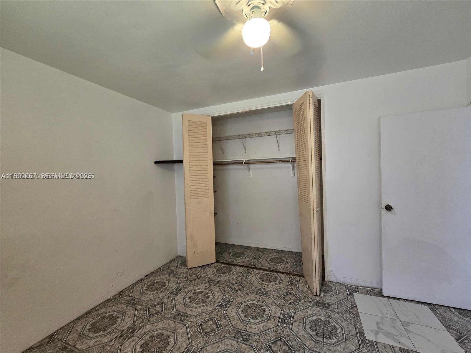 A bedroom features patterned tile flooring, a ceiling fan, and an open closet with shelving — 70 NW 77th St # 11, Miami FL 33150, MIAMI, FL