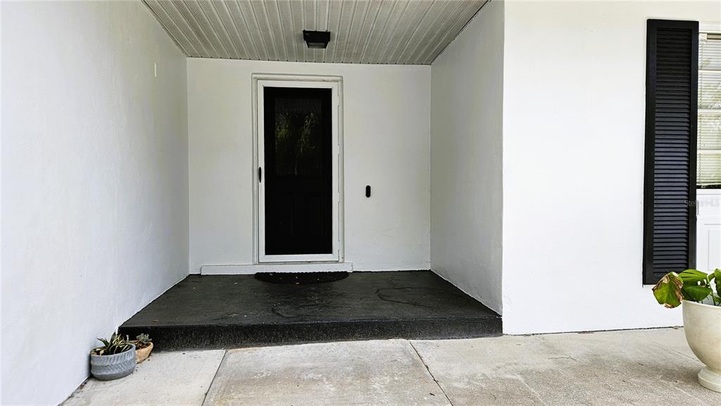 A covered entryway features a black front door, white walls, and a dark concrete porch — 410 BROADVIEW AVENUE, ALTAMONTE SPRINGS, FL
