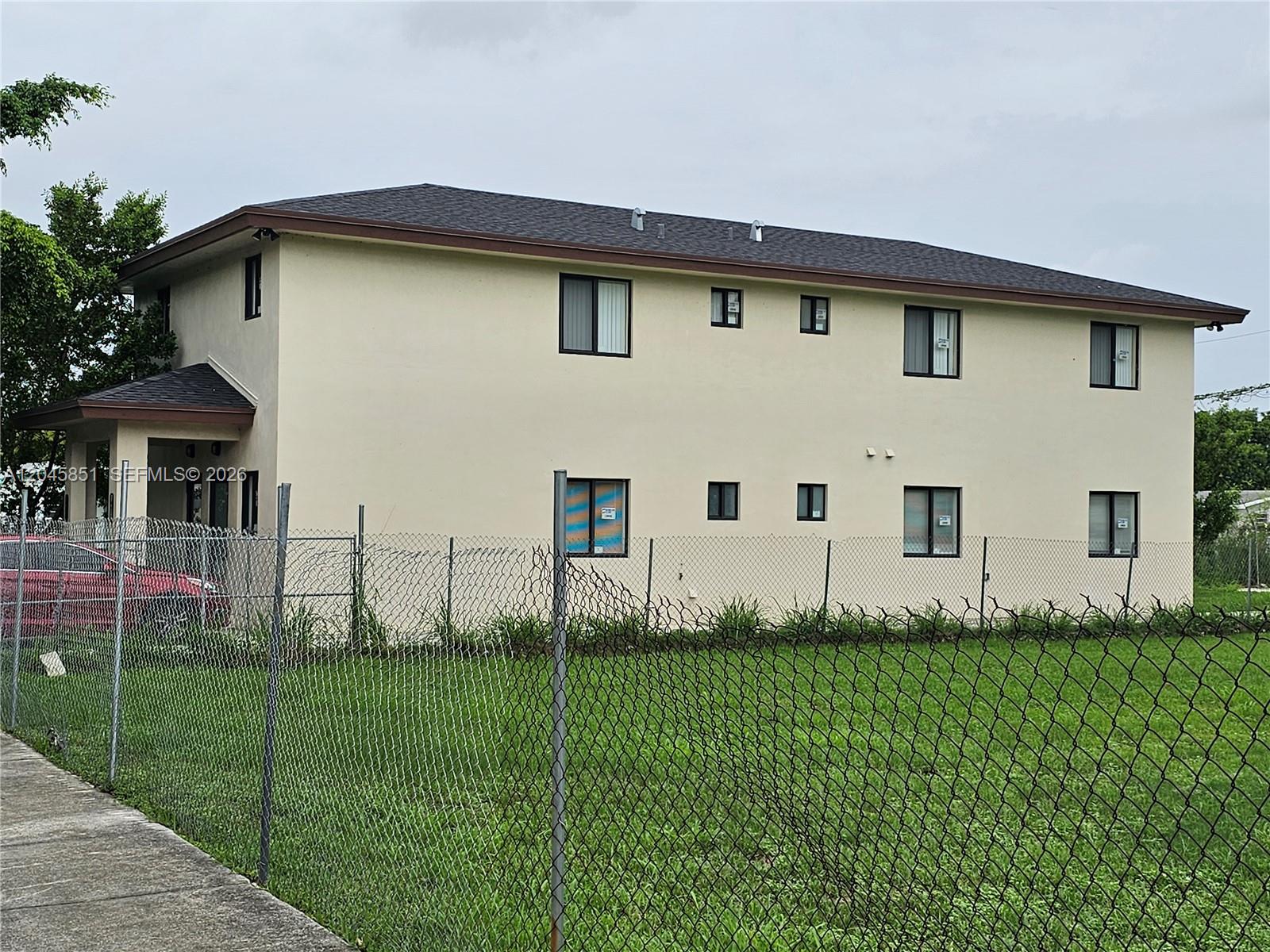 A two-story beige building with a dark roof stands behind a chain-link fence — 10455 SW 179th St # 1, Miami FL 33157, MIAMI, FL