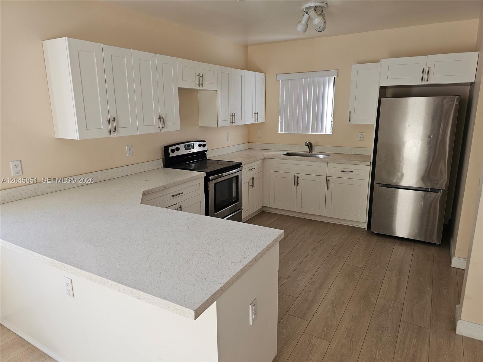 A kitchen features white cabinets, stainless steel appliances, light countertops, and wood-look flooring — 10455 SW 179th St # 1, Miami FL 33157, MIAMI, FL