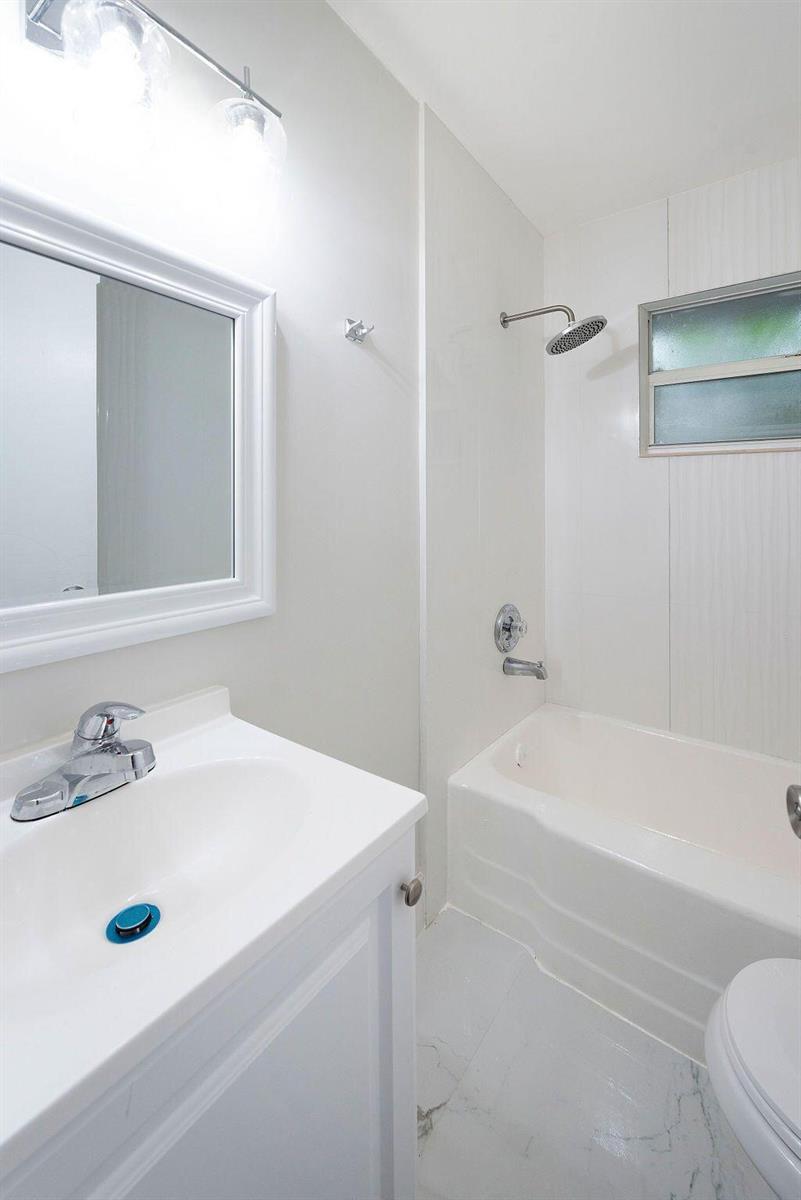 A white bathroom features a vanity with a sink, a mirror, and a shower-tub combination — 1883 Smith Drive # 2, FL 33408, FL