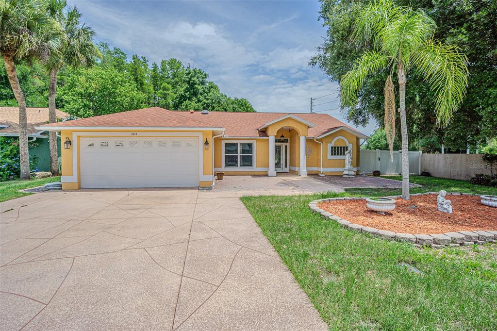 A yellow single-story house with a two-car garage and a paved driveway — 7715 CYPRESS TRACE COURT, NEW PORT RICHEY, FL