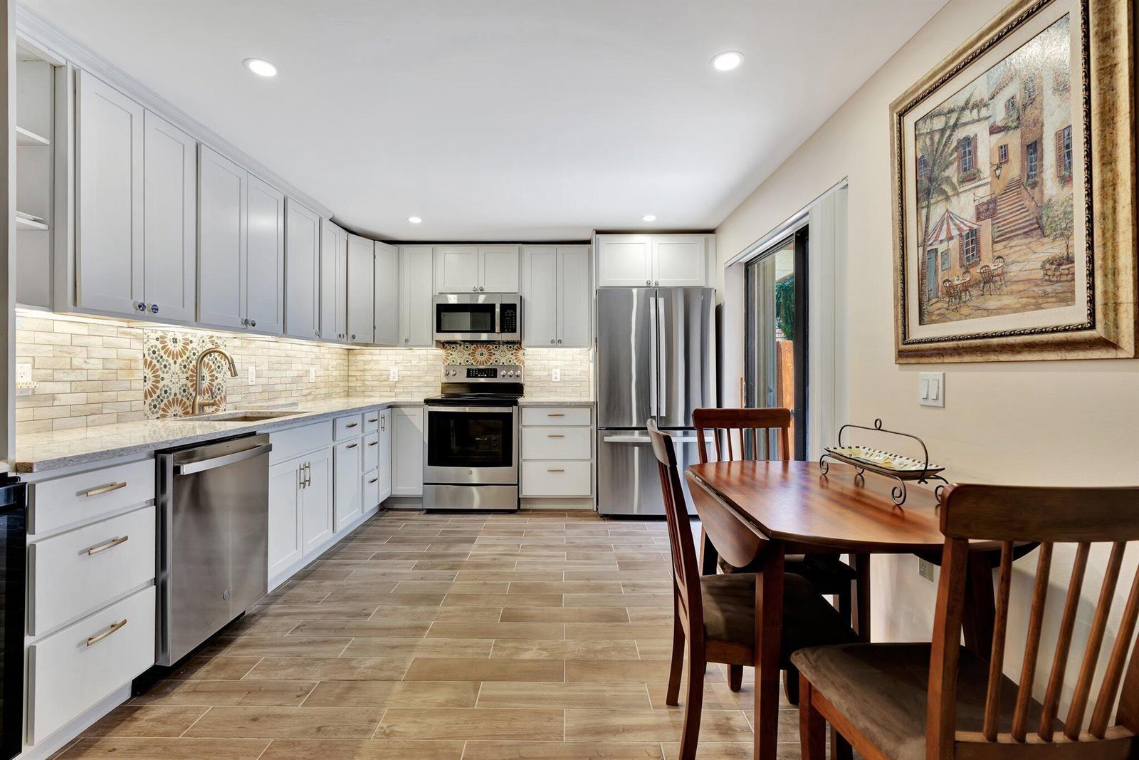 A kitchen with white cabinets, stainless steel appliances, patterned backsplash, and a dining area — 3016 30th Court, Jupiter FL 33477, JUPITER, FL