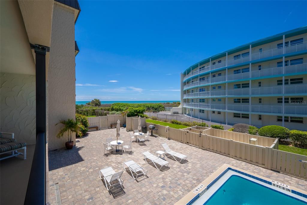 An elevated view of a paved pool deck with lounge chairs, tables, and ocean views — 4100 OCEAN BEACH BOULEVARD UNIT 206, COCOA BEACH, FL