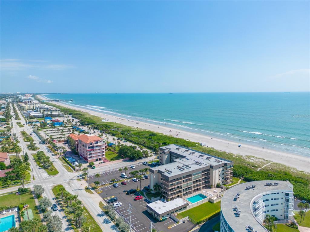 An aerial view shows beachfront condominiums, a parking lot, and a sandy beach along the ocean — 4100 OCEAN BEACH BOULEVARD UNIT 206, COCOA BEACH, FL