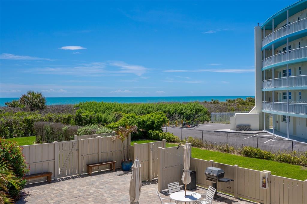 A patio with a grill and dining set overlooks a beach, dunes, and a building — 4100 OCEAN BEACH BOULEVARD UNIT 206, COCOA BEACH, FL