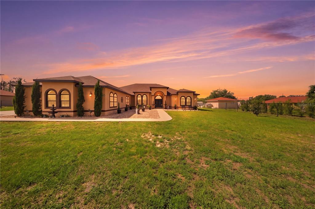 A single-story tan house with arched windows and a large lawn at sunset — 13429 MONTEVISTA ROAD, CLERMONT, FL