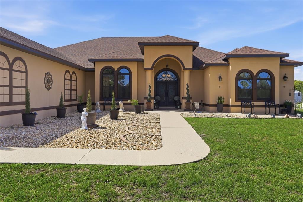 The exterior of a tan stucco house features a stone walkway and arched windows — 13429 MONTEVISTA ROAD, CLERMONT, FL