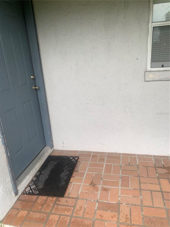 A blue front door opens onto a brick-tiled porch with a black welcome mat — 1674 NE FLORIDIAN CIRCLE, ARCADIA, FL