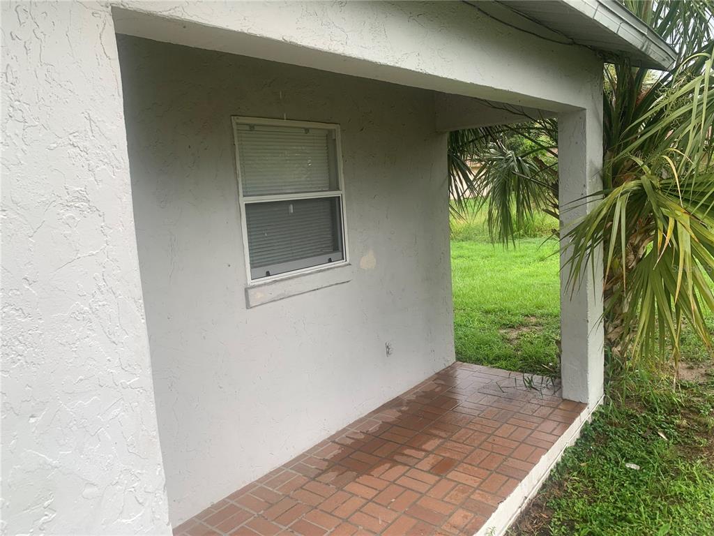 A covered porch features a brick floor, a single window, and a view of grass — 1674 NE FLORIDIAN CIRCLE, ARCADIA, FL