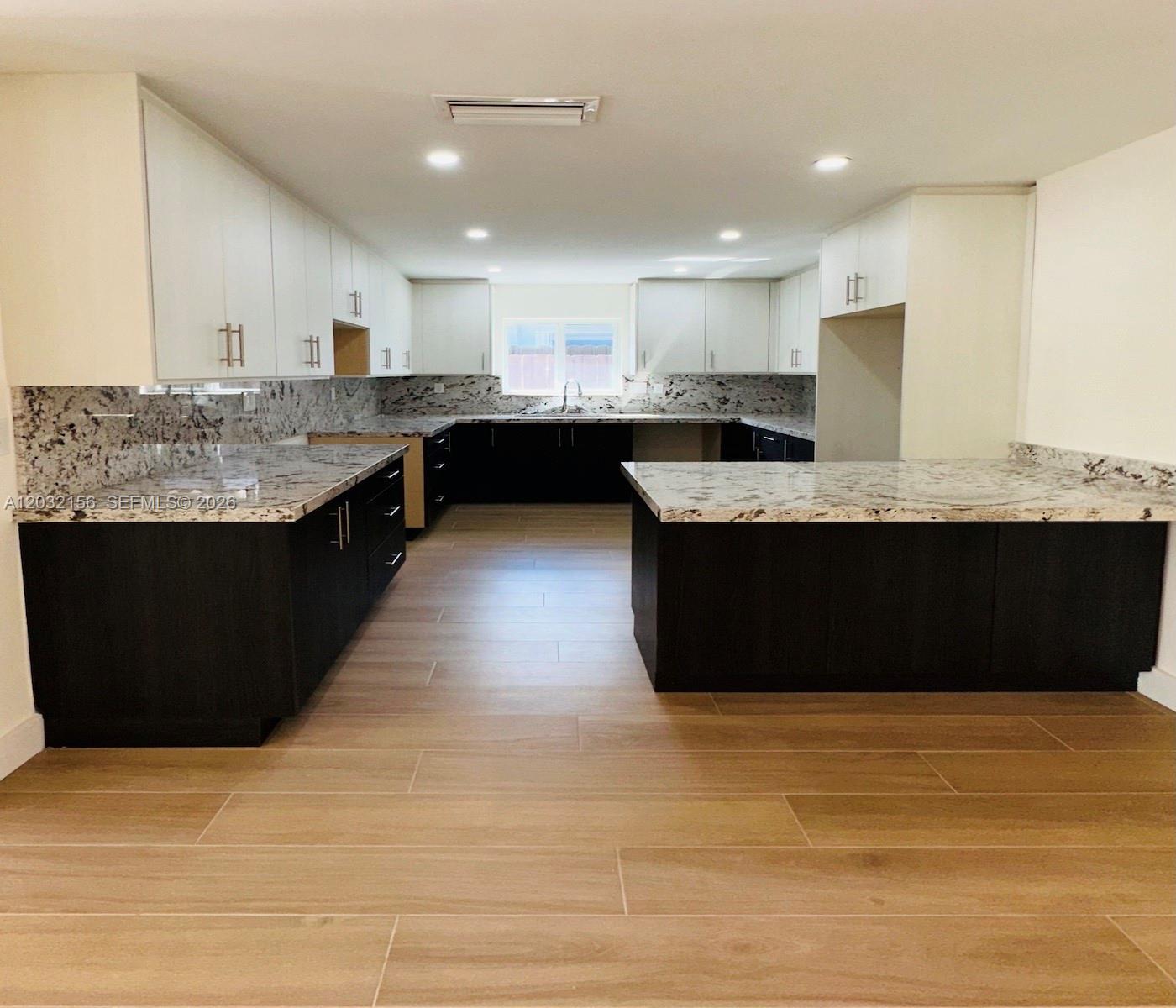 A modern kitchen features dark lower cabinets, white upper cabinets, and granite countertops — 4120 SW 69 Ave, Miami FL 33155, MIAMI, FL