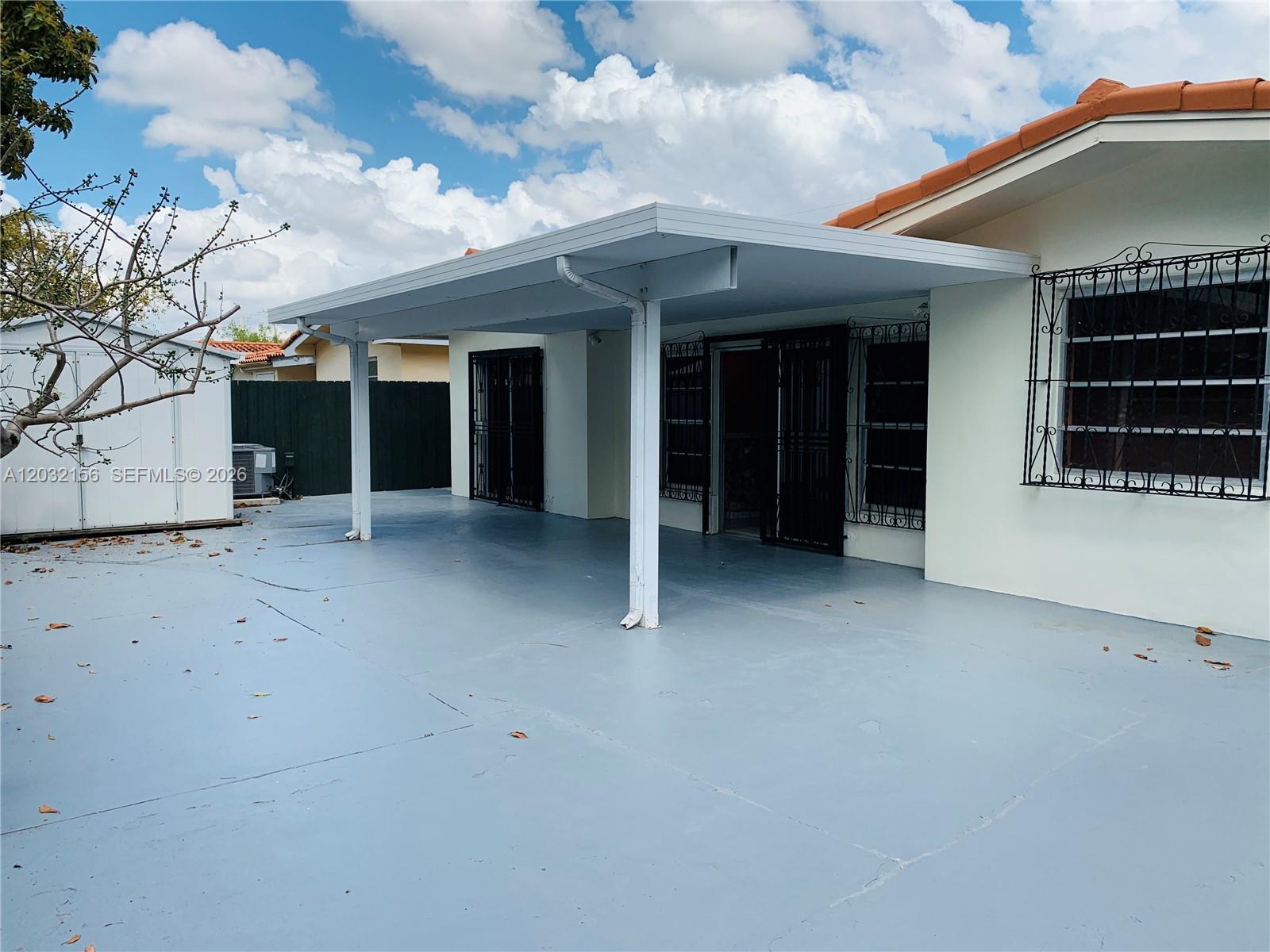 A concrete patio with a covered roof extension sits outside a house with security bars — 4120 SW 69 Ave, Miami FL 33155, MIAMI, FL