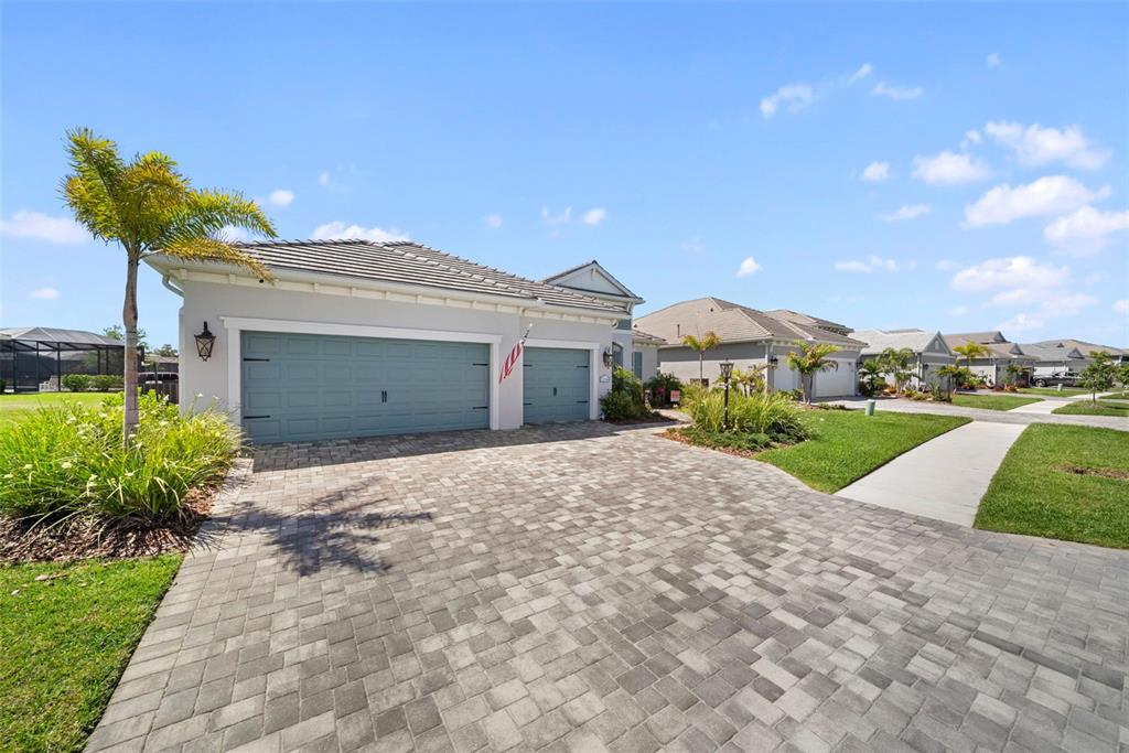 A single-story house with a blue garage, paver driveway, and palm tree under blue sky — 21244 HOLMES CIRCLE, VENICE, FL