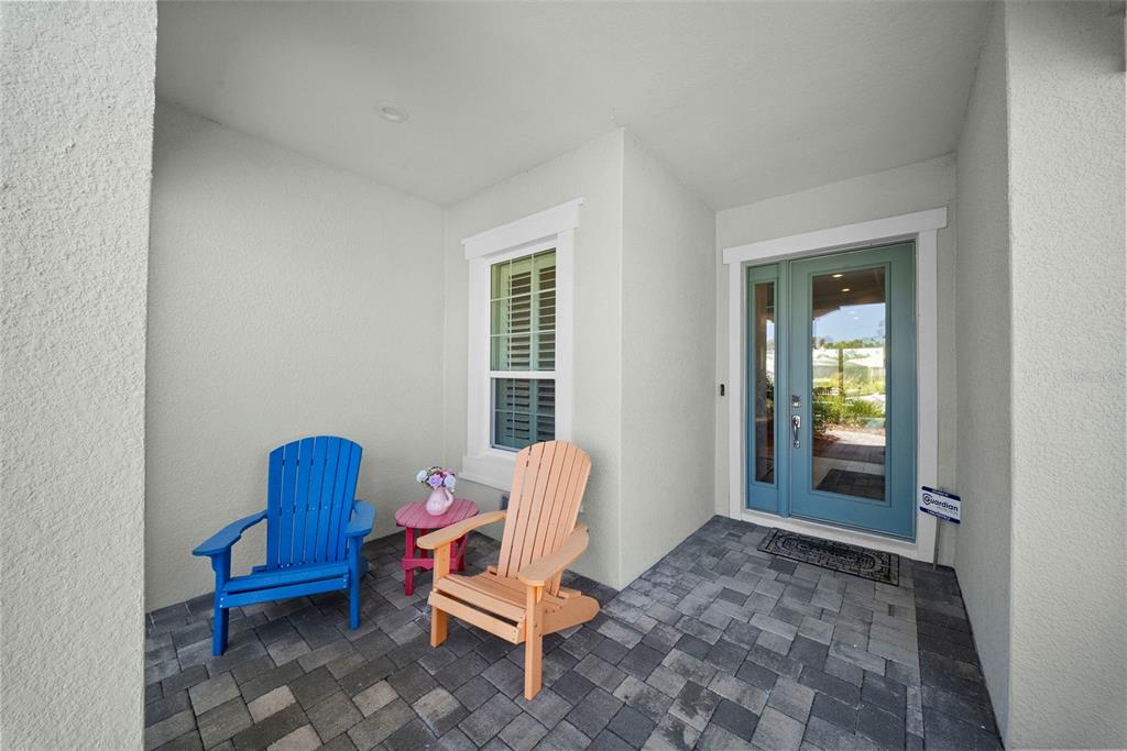 A covered front porch features a paved floor, two Adirondack chairs, and a teal door — 21244 HOLMES CIRCLE, VENICE, FL