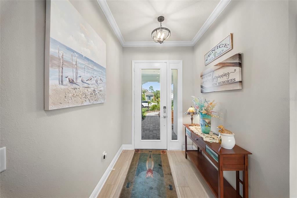 A bright entryway features a wood console table, coastal wall art, and a glass-paneled front door — 21244 HOLMES CIRCLE, VENICE, FL