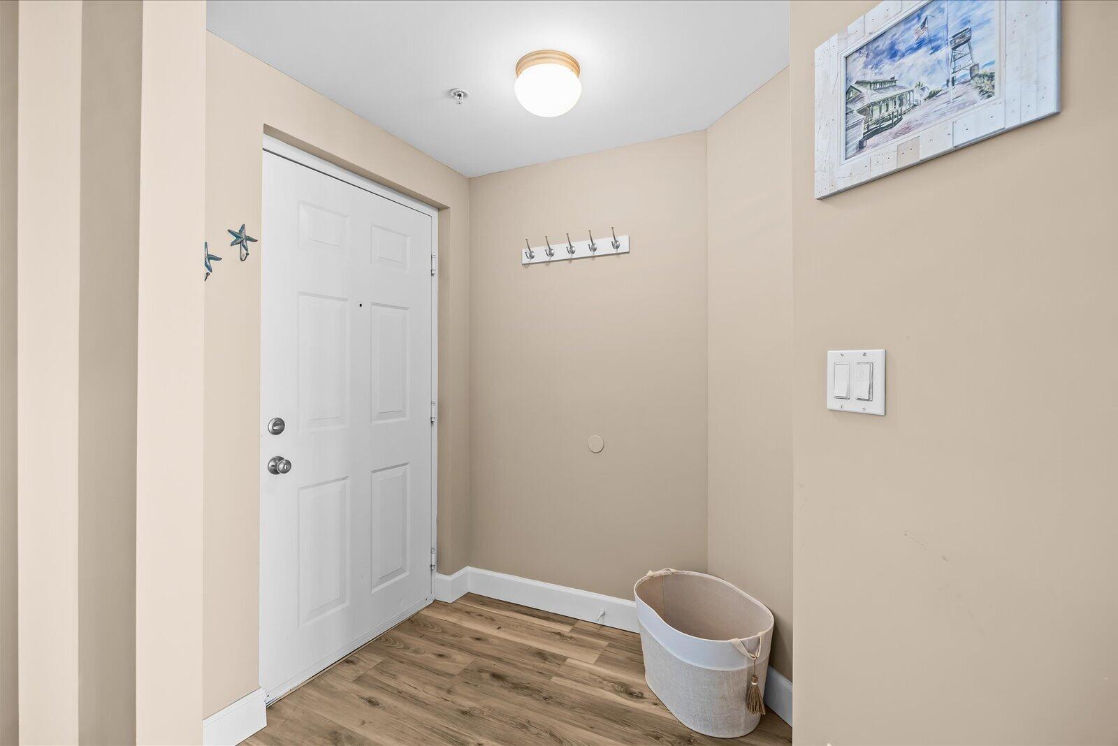 An entryway features a white door, light wood-look flooring, a wall-mounted coat rack, and a basket — 715 NW Flagler Avenue # 302, Stuart FL 34994, STUART, FL