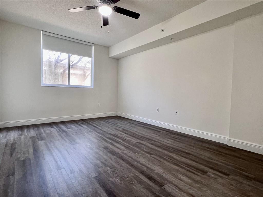 An empty bedroom features dark wood-look flooring, white walls, a ceiling fan, and a window — 18335 NW 68 Avenue # 110, Hialeah FL 33015, HIALEAH, FL