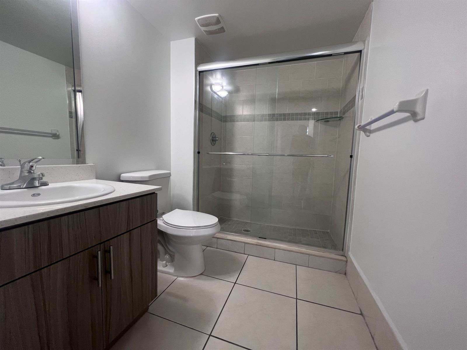 A bathroom features a wood-toned vanity, a white toilet, and a glass-enclosed walk-in shower — 18335 NW 68 Avenue # 110, Hialeah FL 33015, HIALEAH, FL
