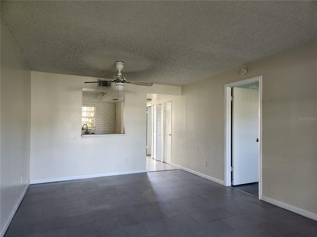 A living room features gray tile flooring, a ceiling fan, and a kitchen pass-through window — 6122 7TH AVENUE W, BRADENTON, FL