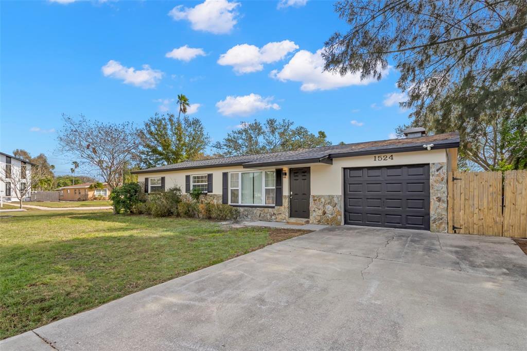A single-story house with a stone facade, dark garage door, and a concrete driveway — 1524 ARIZONA AVENUE NE, ST PETERSBURG, FL