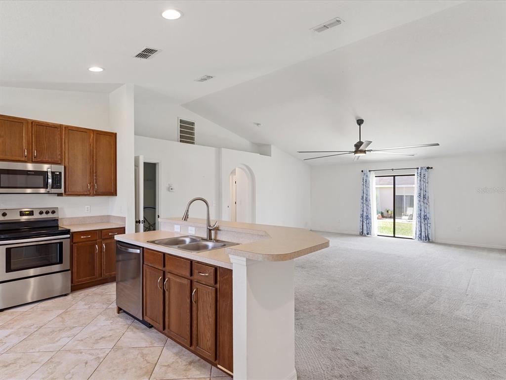 A kitchen with wood cabinets and a breakfast bar opens into a carpeted living area — 630 VALENCIA COURT, DUNDEE, FL
