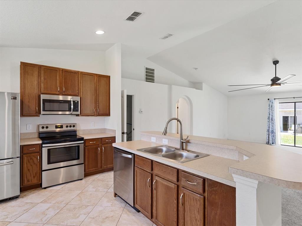 A kitchen with wood cabinets, stainless steel appliances, and a peninsula sink overlooking a living area — 630 VALENCIA COURT, DUNDEE, FL
