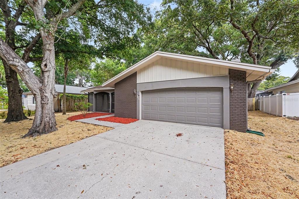 A single-story house with a brown brick exterior, a two-car garage, and large oak trees — 2431 GROVE RIDGE DRIVE, PALM HARBOR, FL